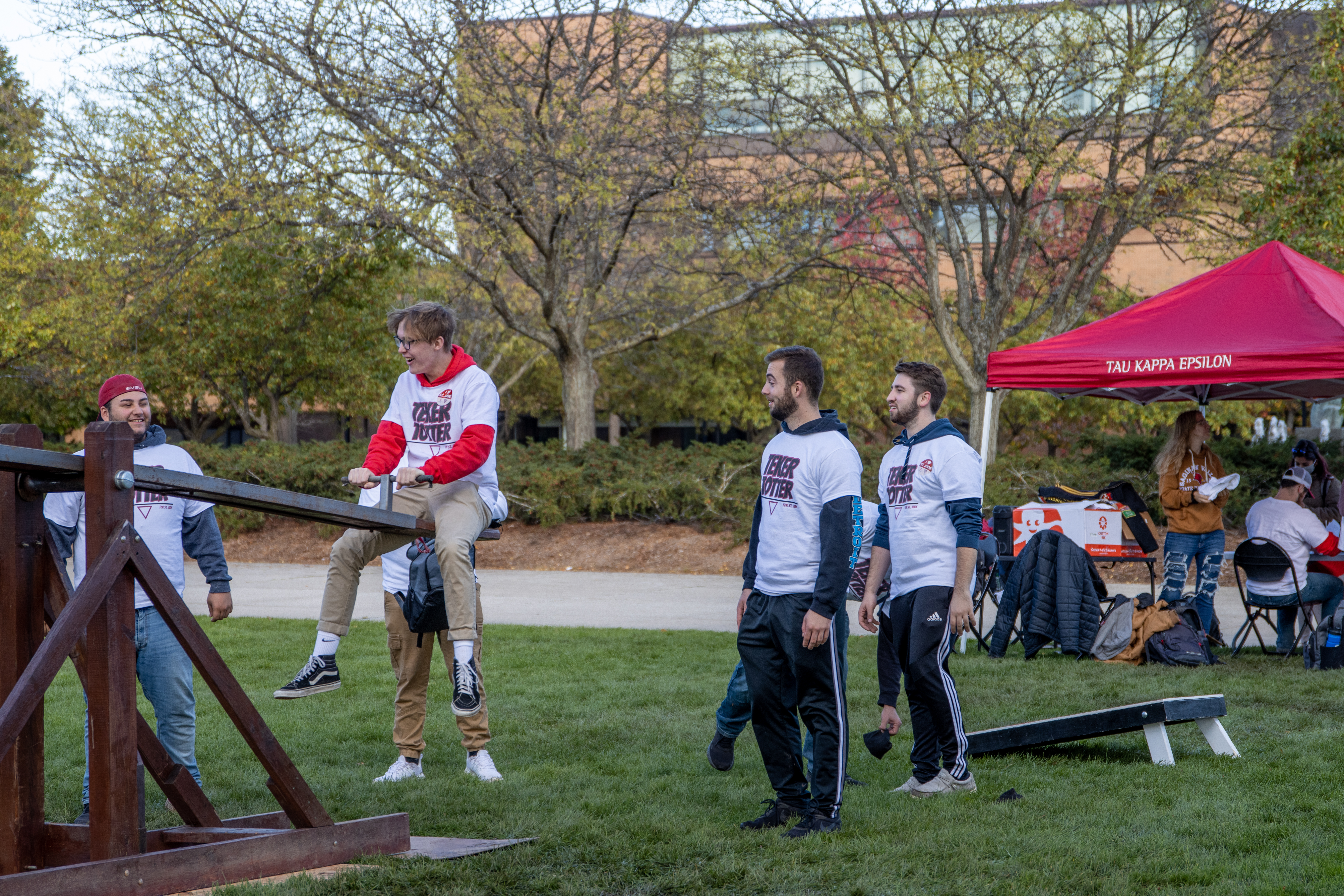 Students watching another student on the teeter totter for the Tau Kappa Epsilon event for charity.